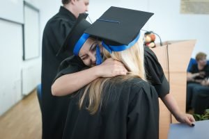 Two girls in caps and gowns hugging on graduation day, aiming towards finding a job in Sarasota