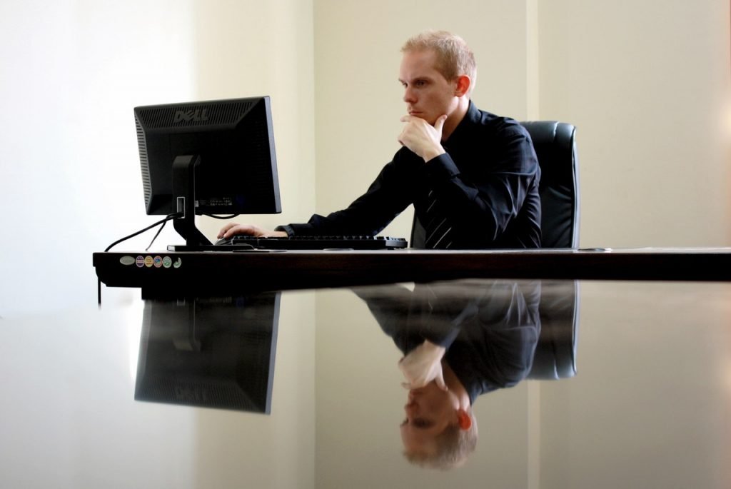 A man sitting in a desk chair working on his desktop computer 