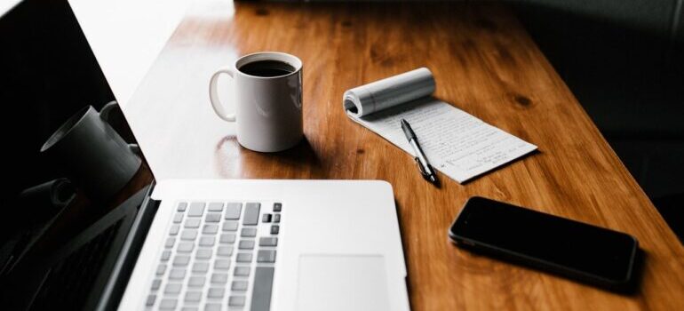 A laptop next to a pen and paper, a cup of coffee, and a smartphone.