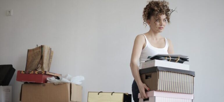 A woman carrying stacks of items next to boxes.