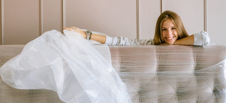 A woman wrapping her couch in see-through tape.