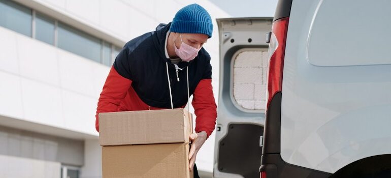 male with a face mask, loading a moving van with cardboard boxes