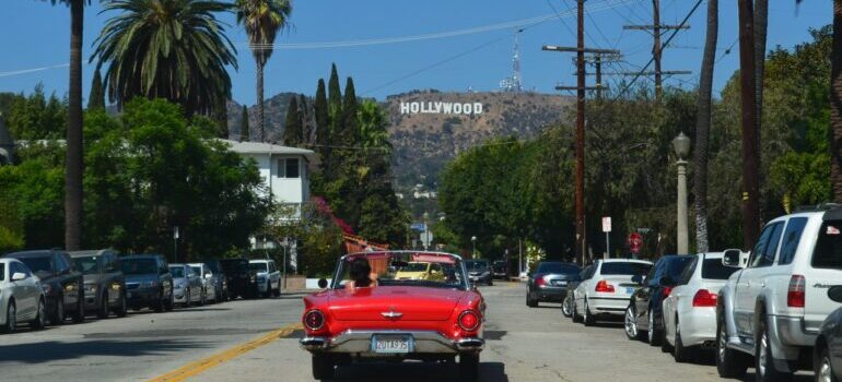Red car on the street with the Hollywood sign on the hill.