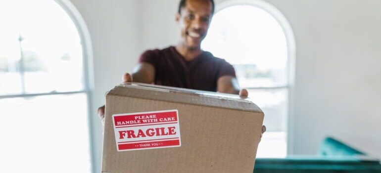 A worker holding a cardboard box with label saying that its fragile.