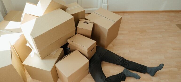 Man laying on the floor covered with the bunch of boxes. 