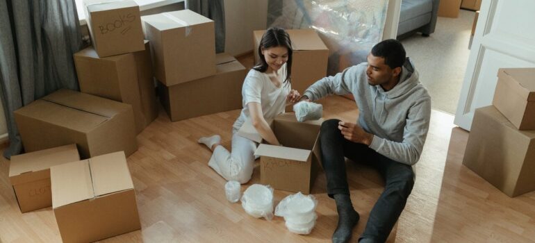 a couple sitting in their living room with boxes all around them