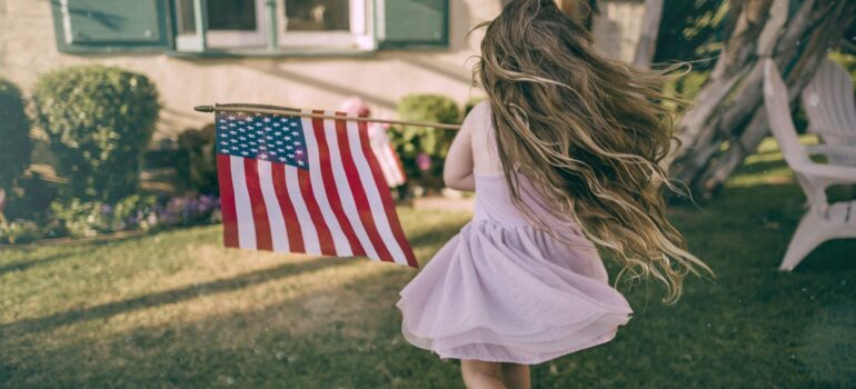 a little girl waving an American flag while running in the backyard