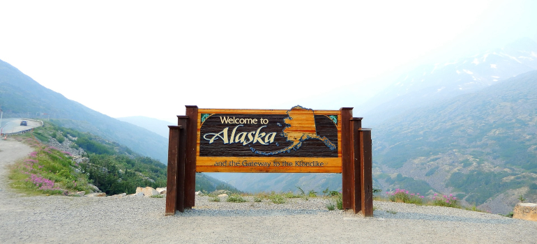 a picture of a welcome sign in Alaska, with a mountain range behind it