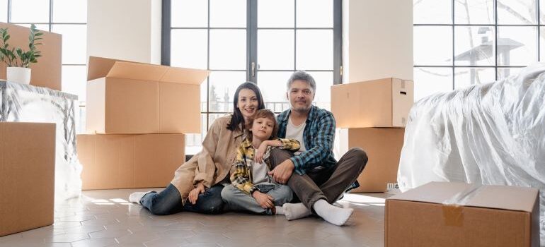 A family of three sitting on the floor, surrounded by boxes.