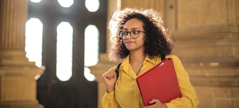 a young woman in a yellow jacket and a red folder in a University building