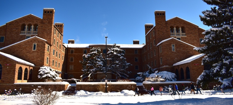 the University of Colorado, Boulder covered in snow with people walking in front of it