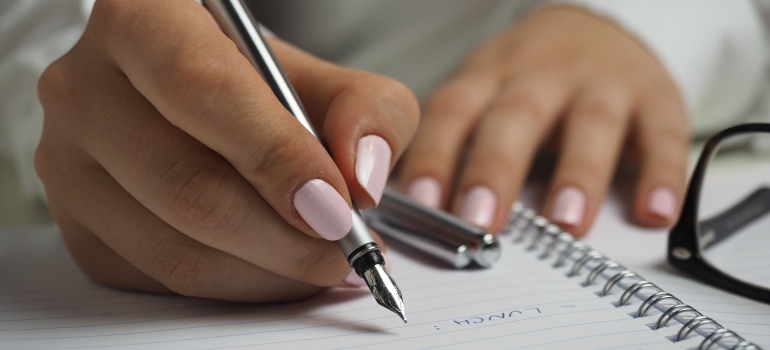 a woman's hands writing on a notebook with a pen