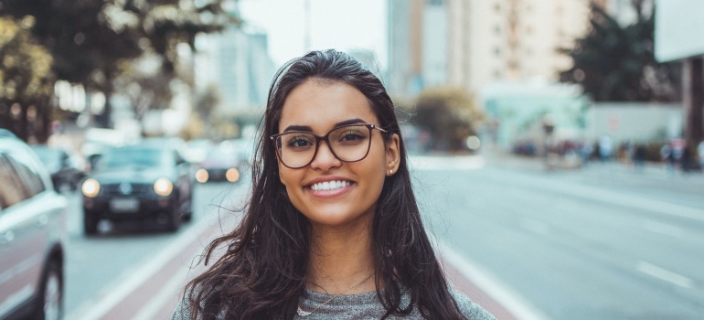 a woman with glasses smiling and standing on a street