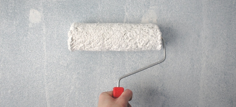 Person holding paint roller on the wall - first thing to do when moving into a new house is to check the damages and repair them.