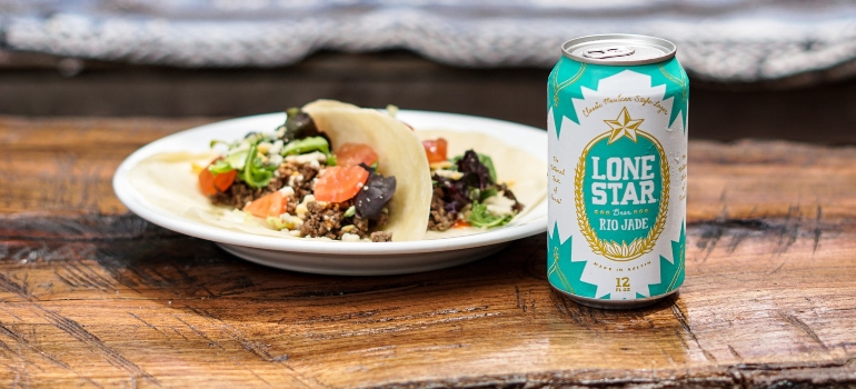 Plate of beef tacos on flour tortillas with a cold Lone Star Rio Jade beer on top of a rustic wood outdoor table.