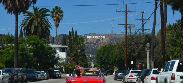 a red car driving in a street towards the Hollywood sign