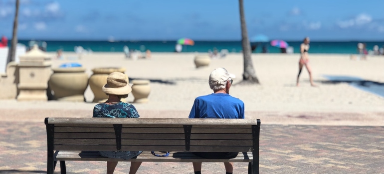 an elderly couple sitting on a bench in a beach