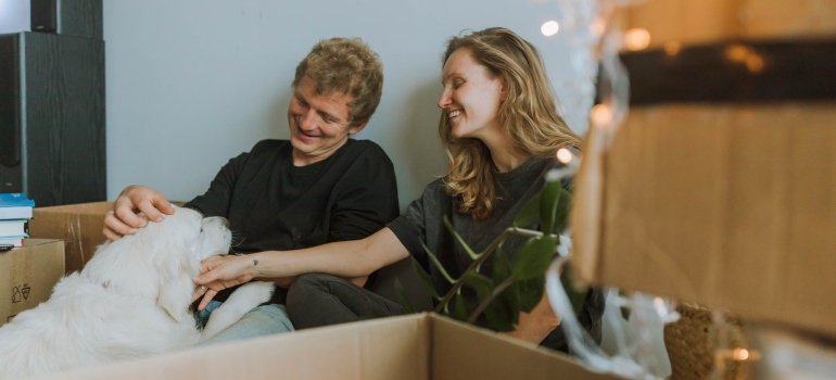 a man a woman and a dog smiling surrounded by cardboard boxes
