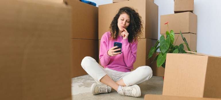 a woman in a pink sweater looking at her phone surrounded by boxes
