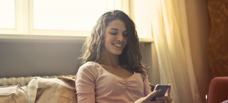 a woman looking at her phone and smiling while on a couch