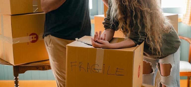 A moving box with fragile items in it with two people over it