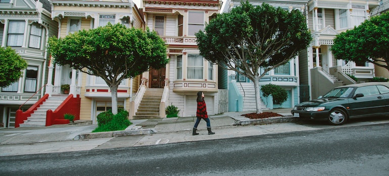 Woman Walking Toward Black Sedan Parked In Front of Colorful Houses.