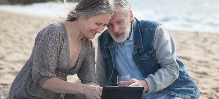 a man and a woman on the beach looking at a tablet